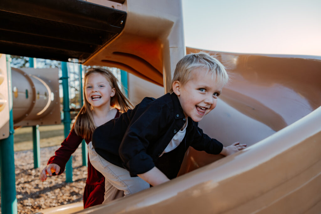 Brother and sister running up a colorful slide in Chicago, surrounded by a vibrant play area.