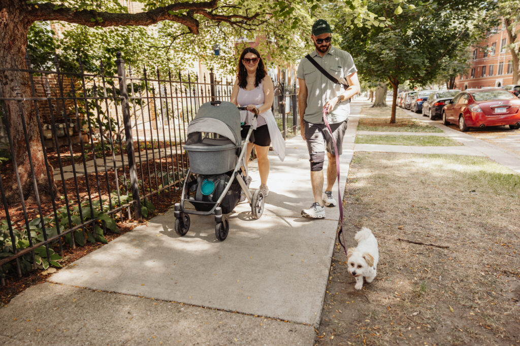 New mom and dad pushing a stroller along the sidewalk in family friendly park in chicago