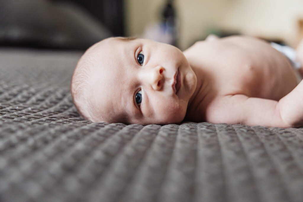Baby laying on bed in home newborn photography session by Taylor Lynn Studios